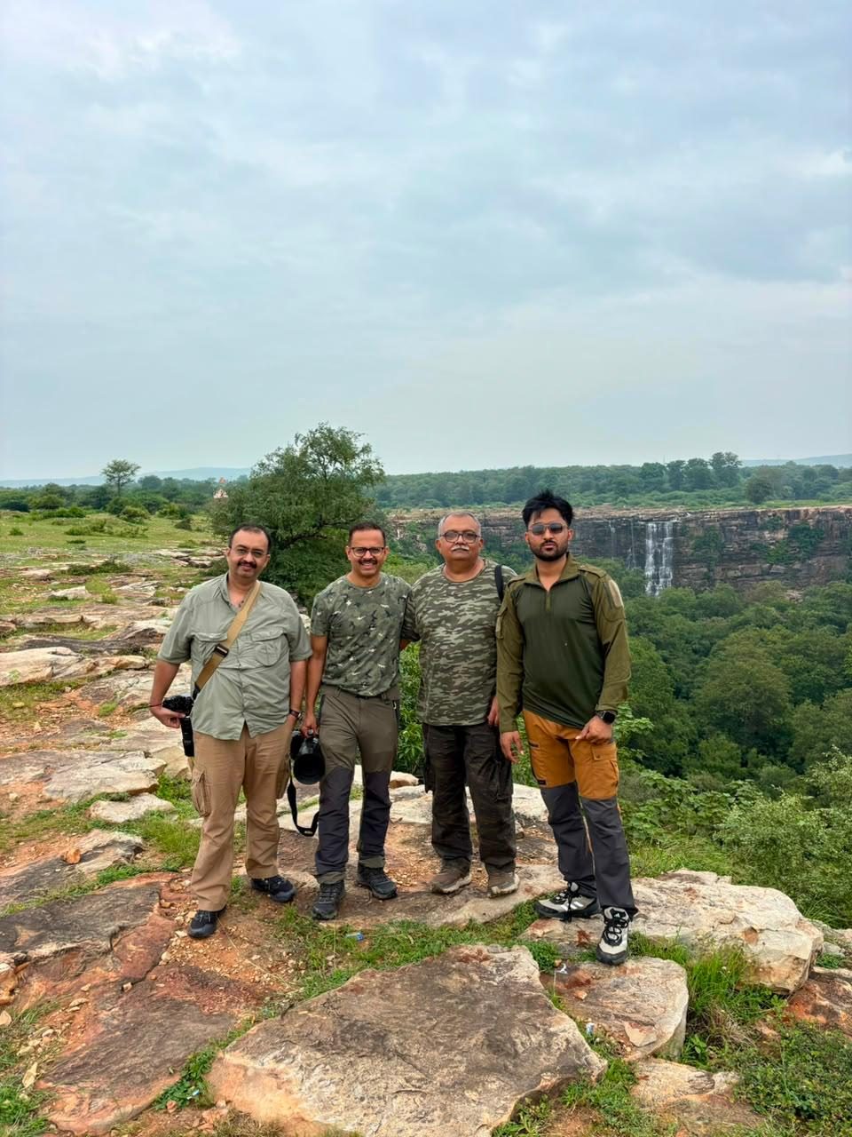 Ashwin Tak and three guests standing on a rocky ledge above a forest waterfall